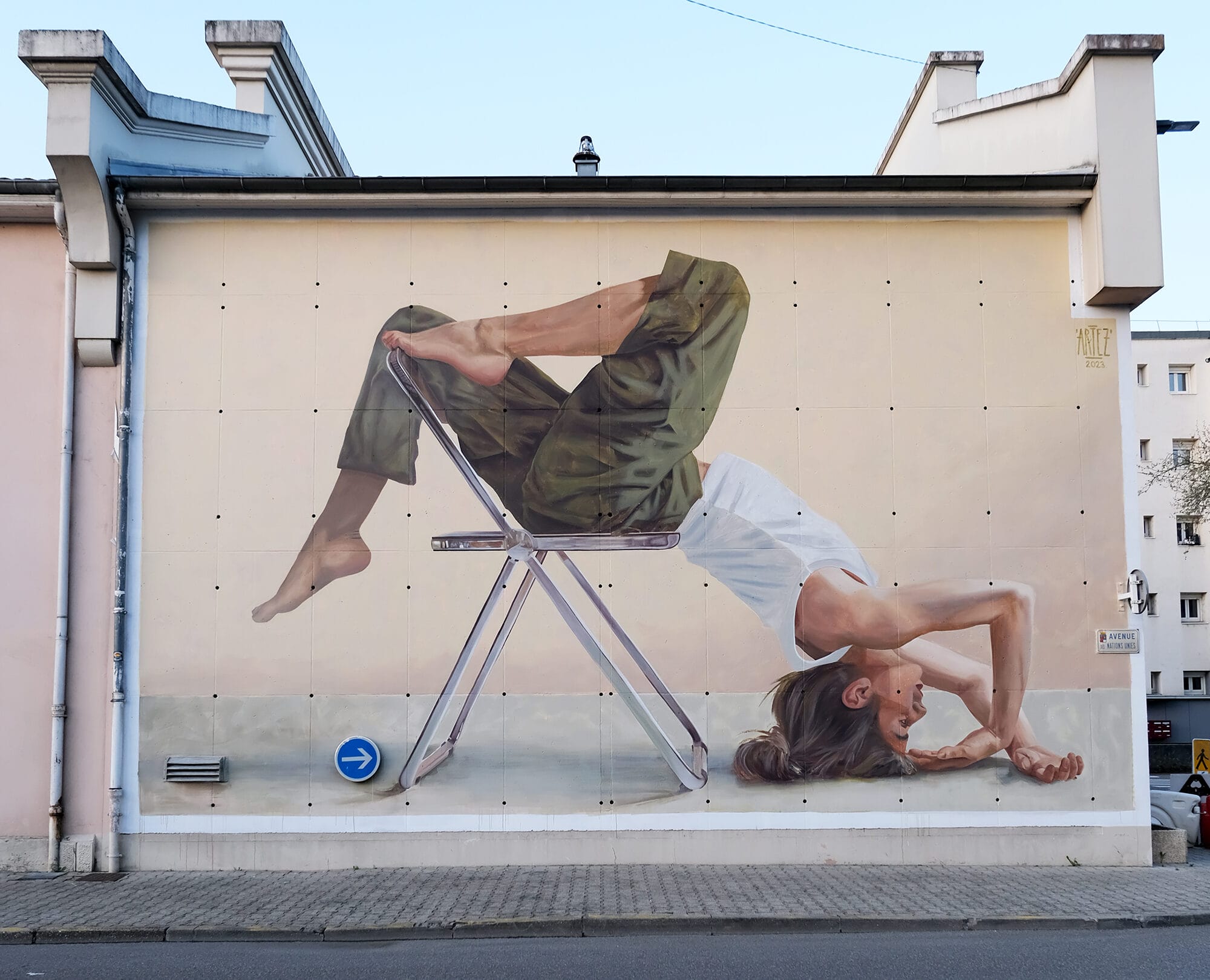 a mural on the side of a residential building of a dancer in an acrobatic pose with a metal chair