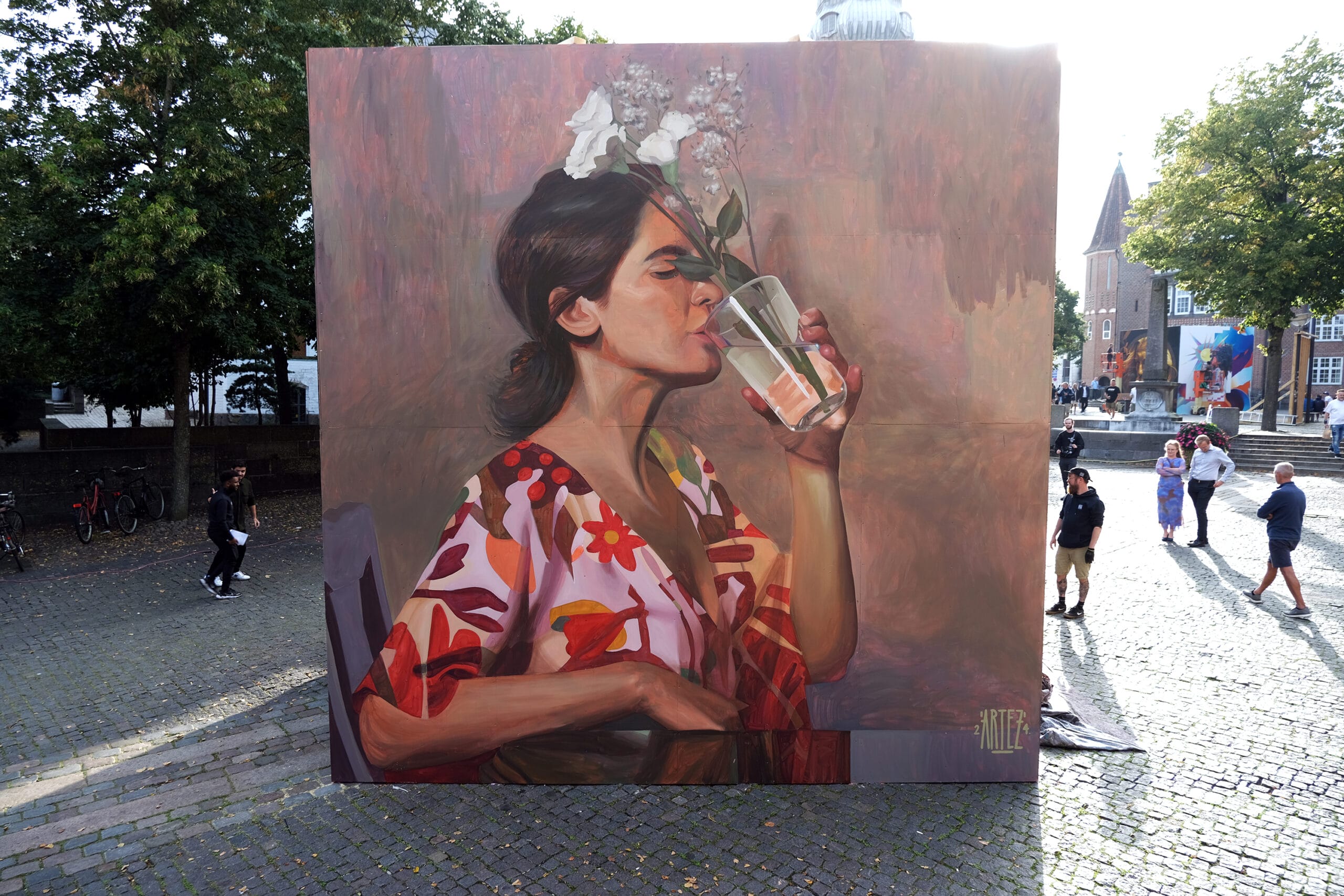 a mural on the side of a building of a woman drinking out of a vase of flowers