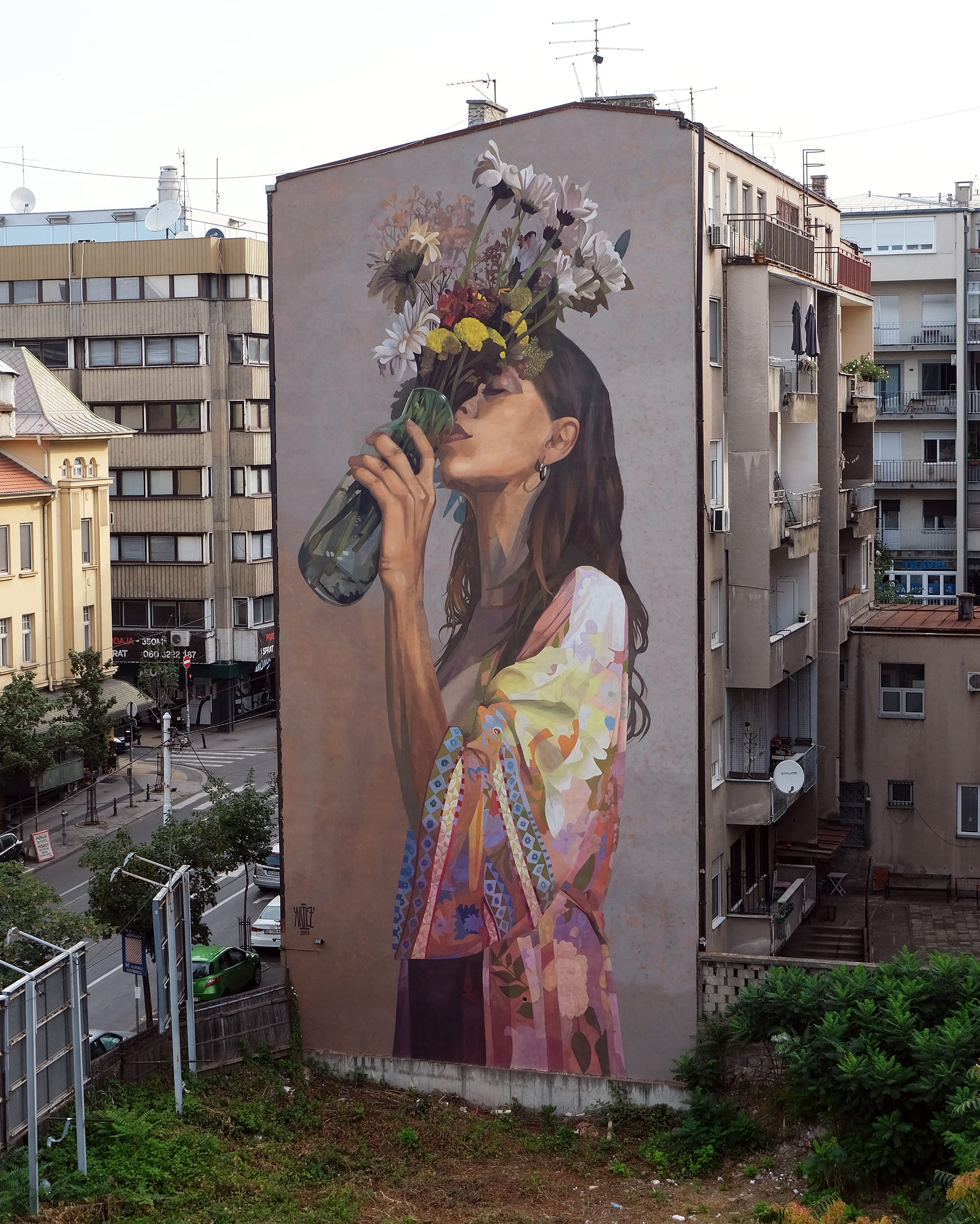 a mural on the side of a tall residential building of a woman drinking out of a vase of flowers