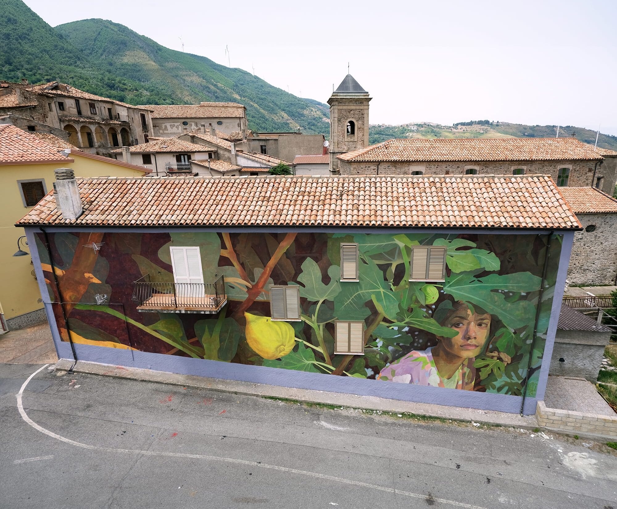 a mural on the side of a residential building of a woman peering out from beneath green foliage