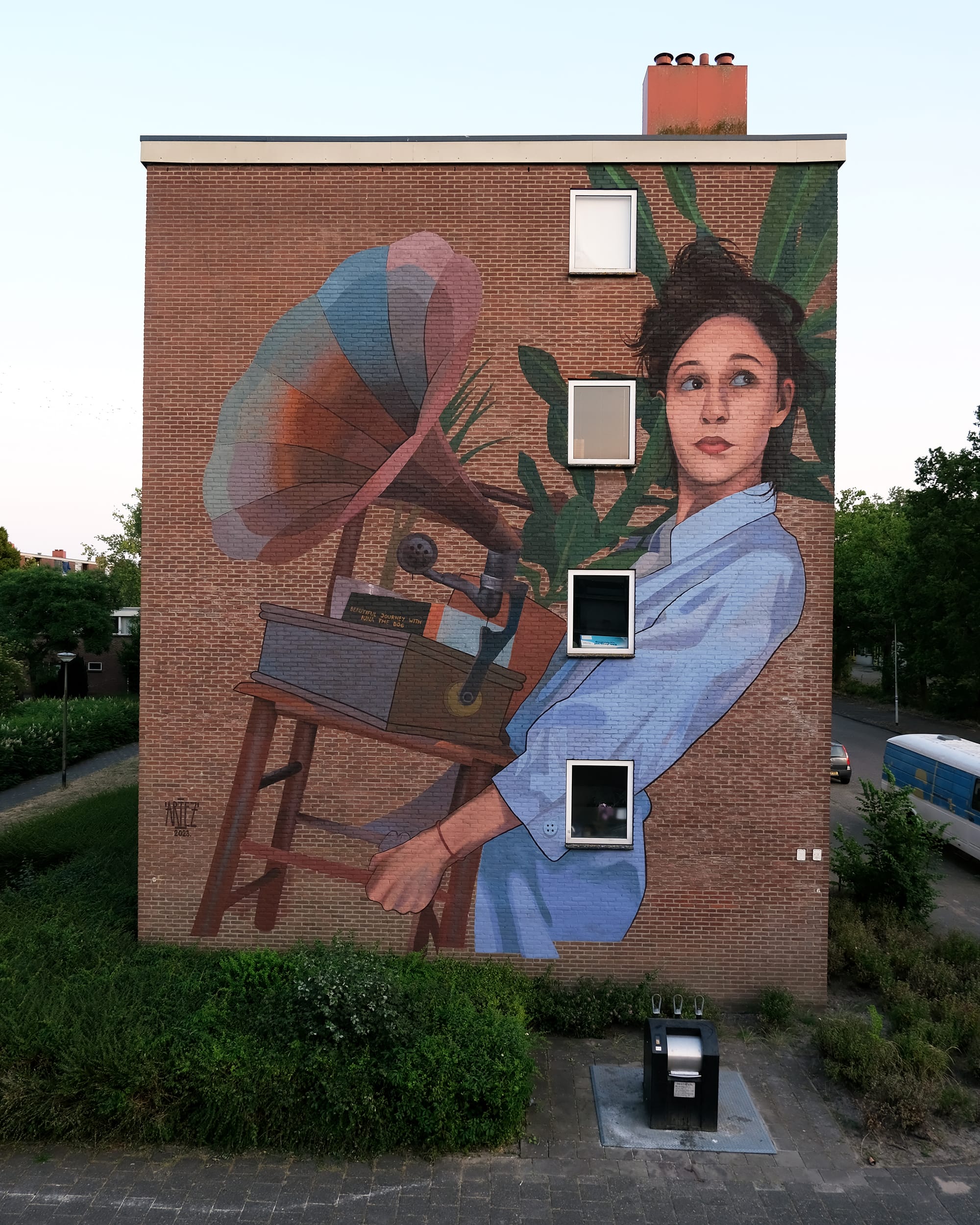 a mural on the side of a residential building of a woman carrying a gramophone and a houseplant