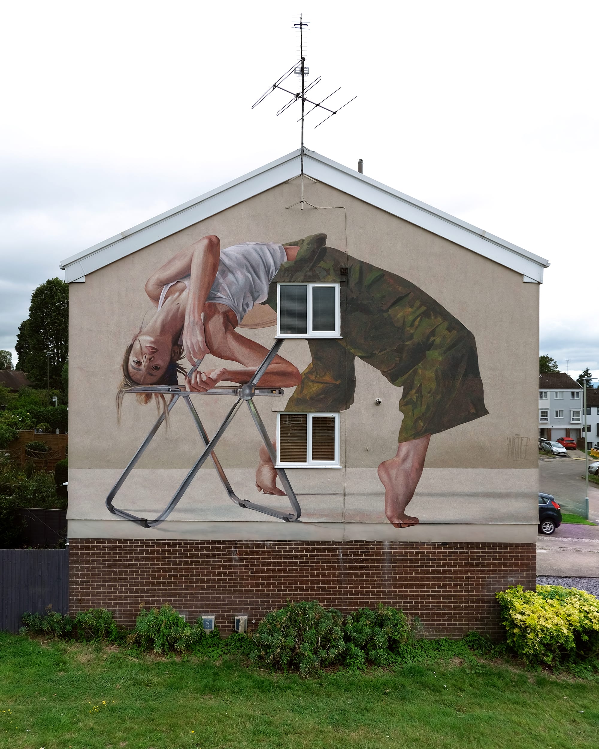 a mural on the side of a residential building of a dancer balancing on a small stool