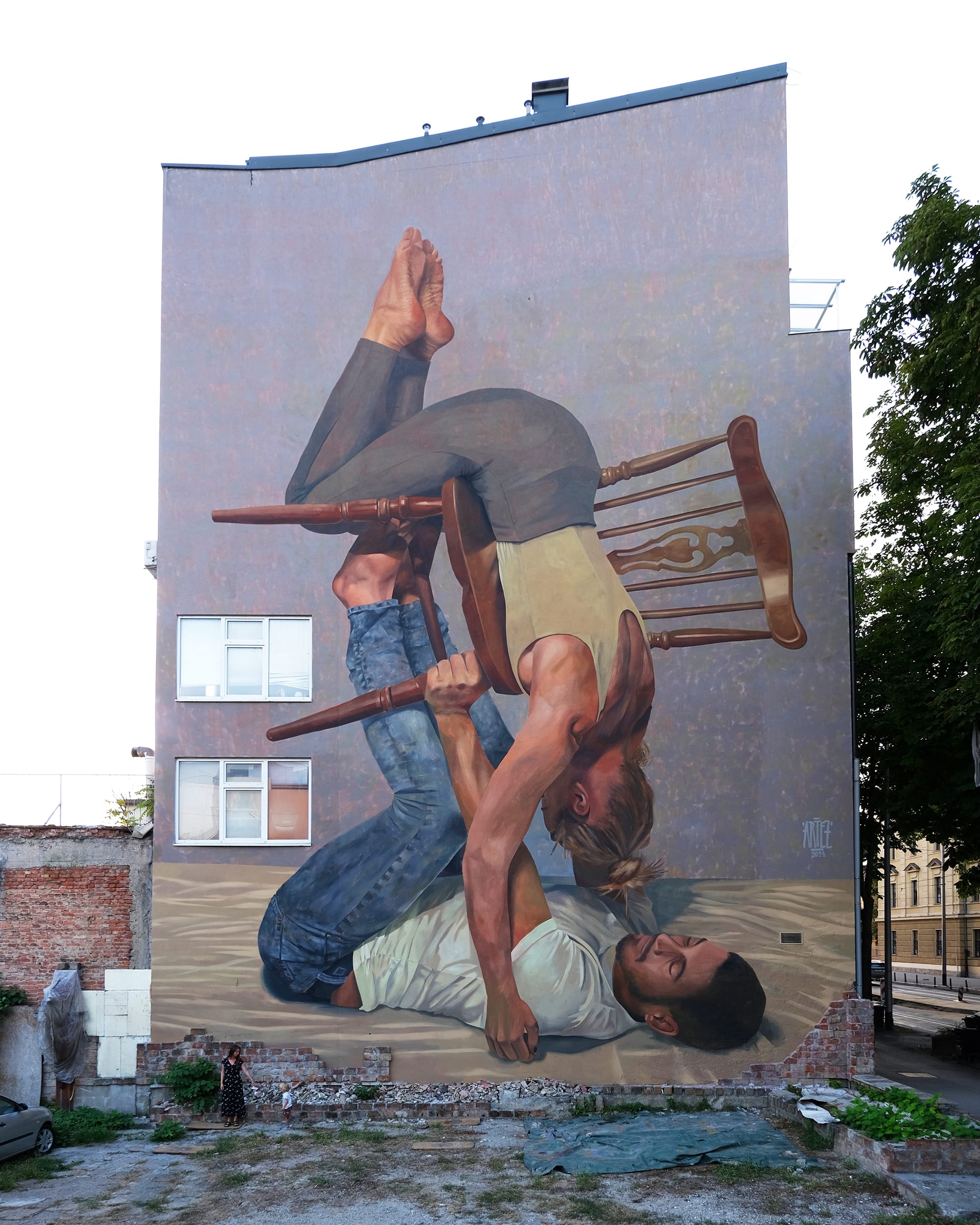 a mural on the side of a residential building of two dancers in an acrobatic pose with a wooden chair