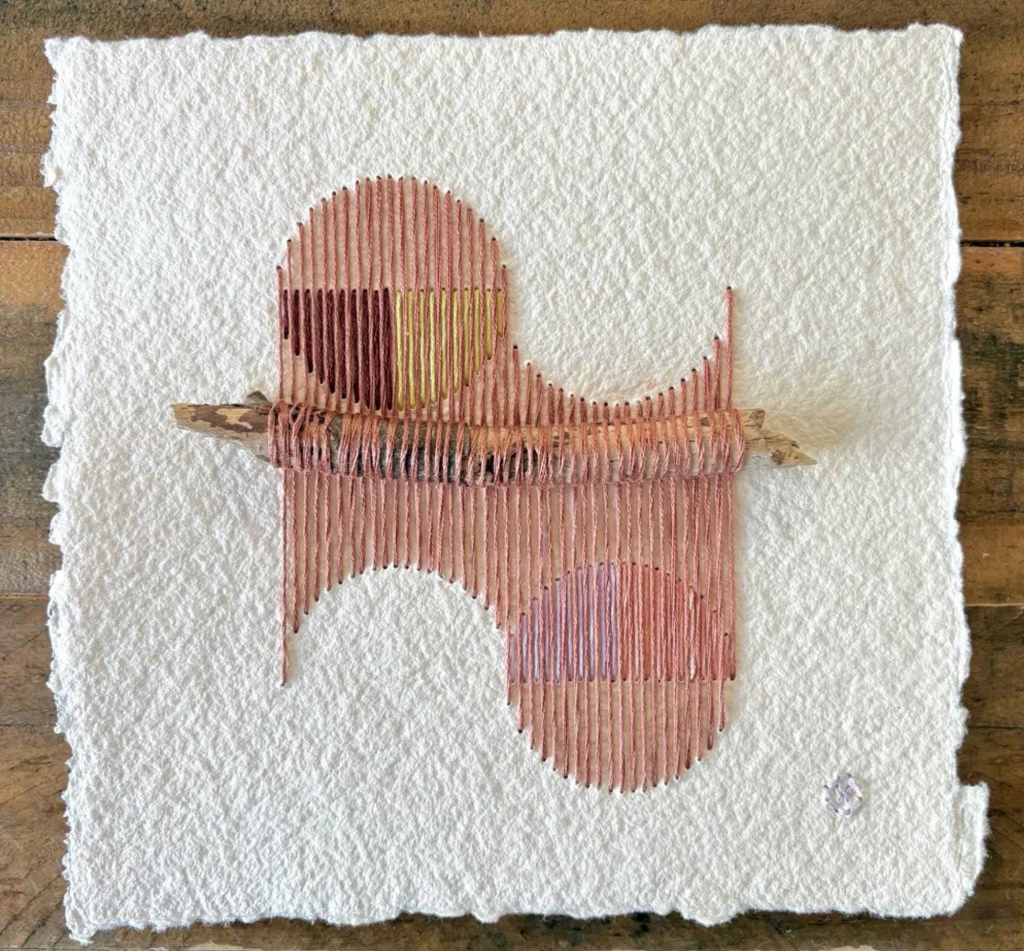a paper artwork by Natalie Ciccoricco featuring handmade paper and pink thread wound around found twigs in a geometric shape