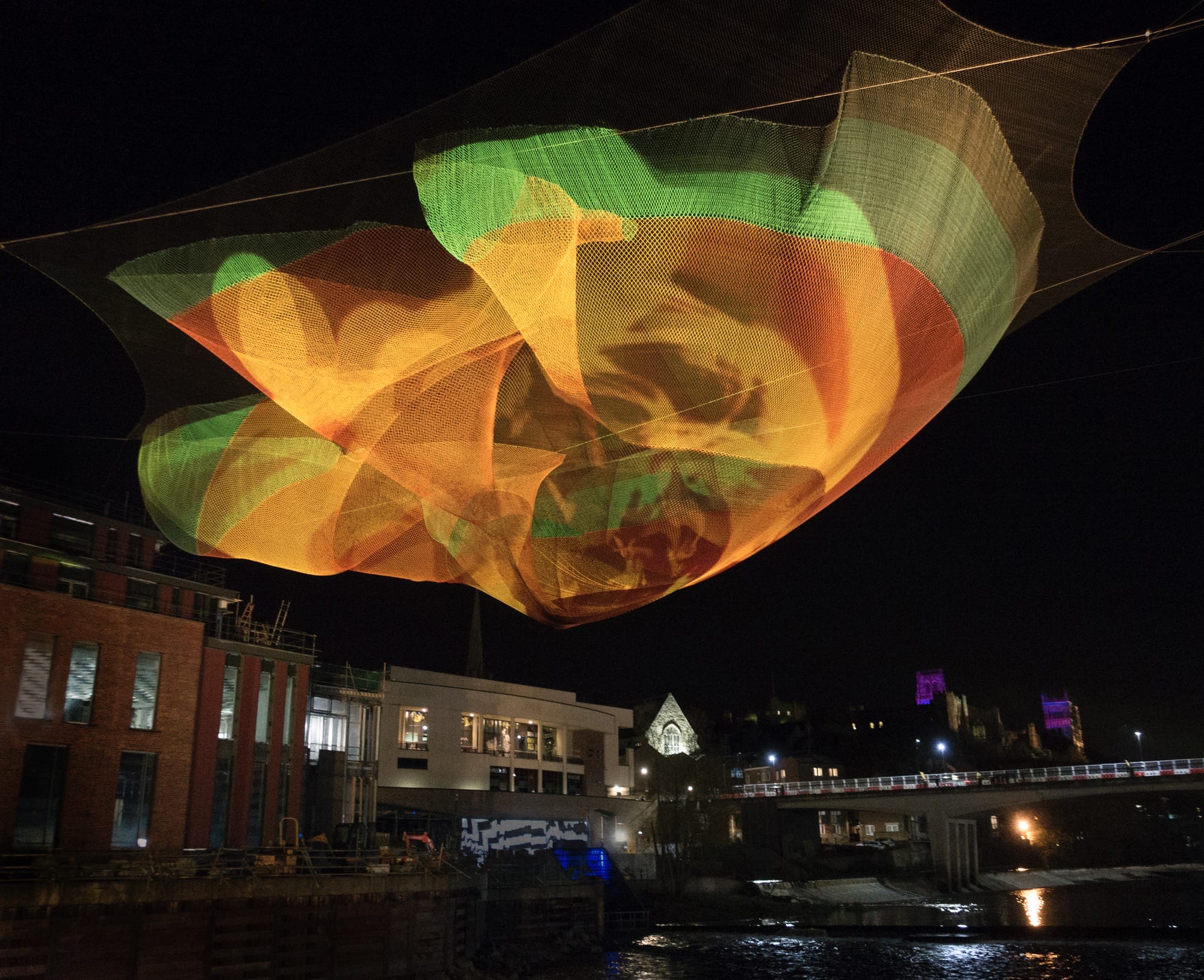 an orange and green Janet Echelman installation suspended in the air