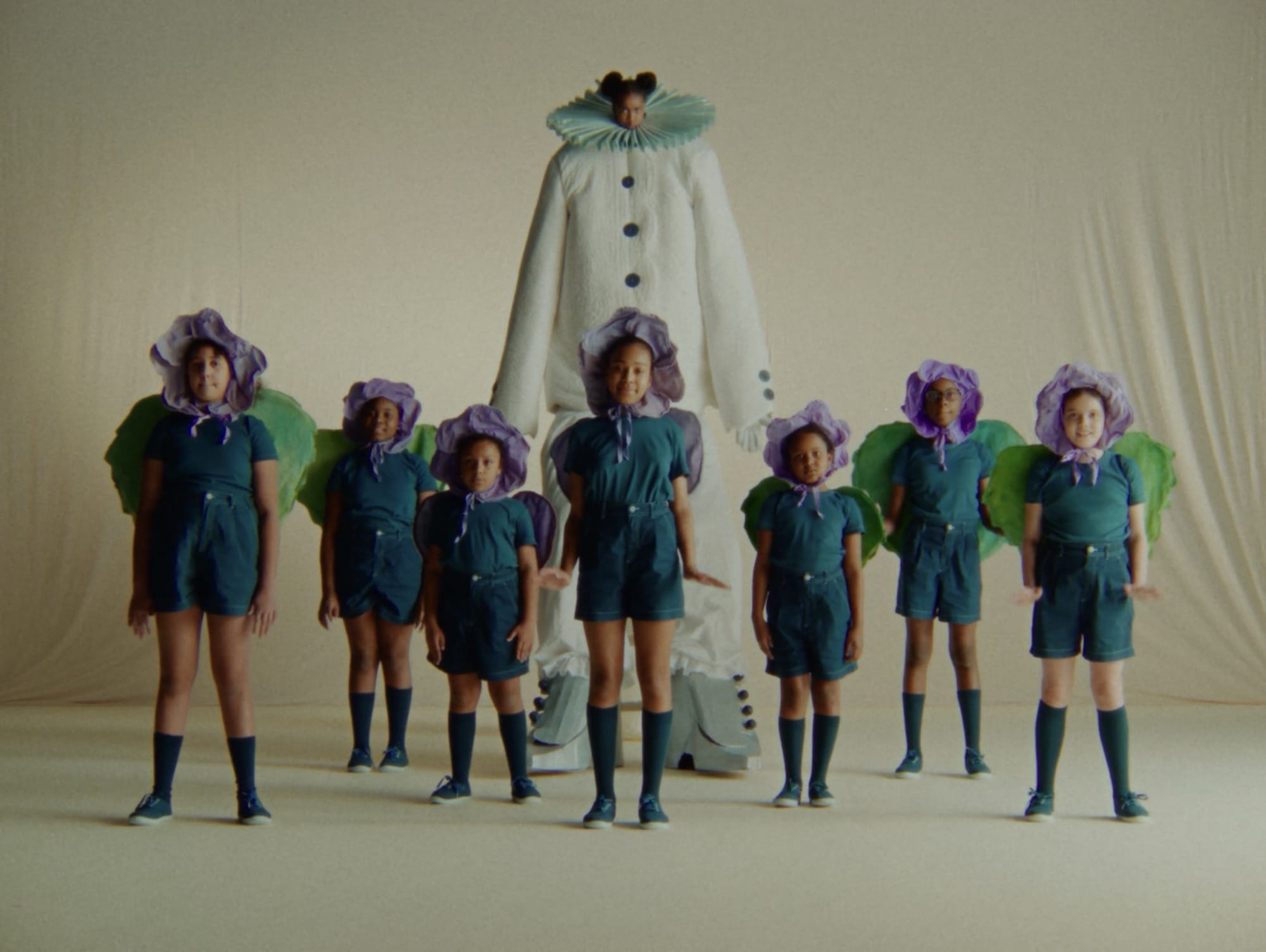 a still from a video titled "A Ffern Fairytail" featuring children in flower costumes and one tall costume of a "frost queen"