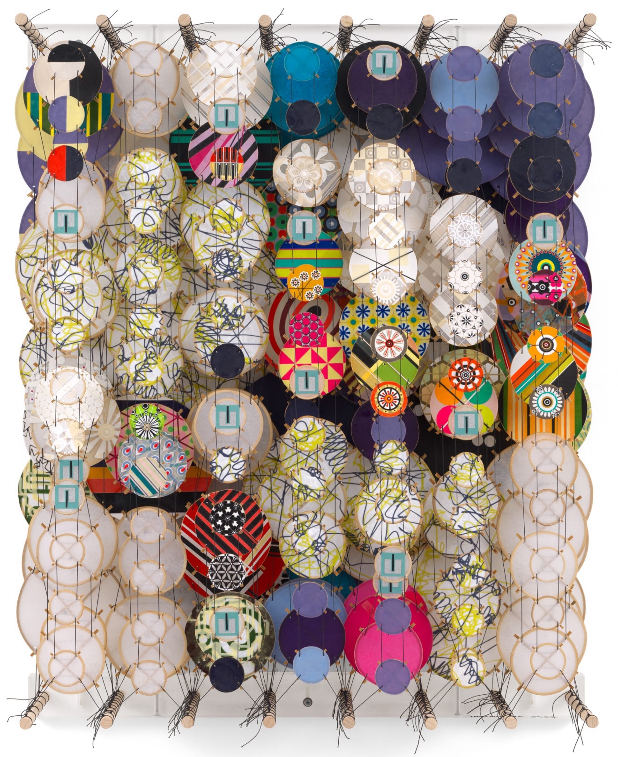 an abstract artwork by Jacob Hashimoto made from twine and numerous colorful, patterned paper discs installed in rows for a layered effect
