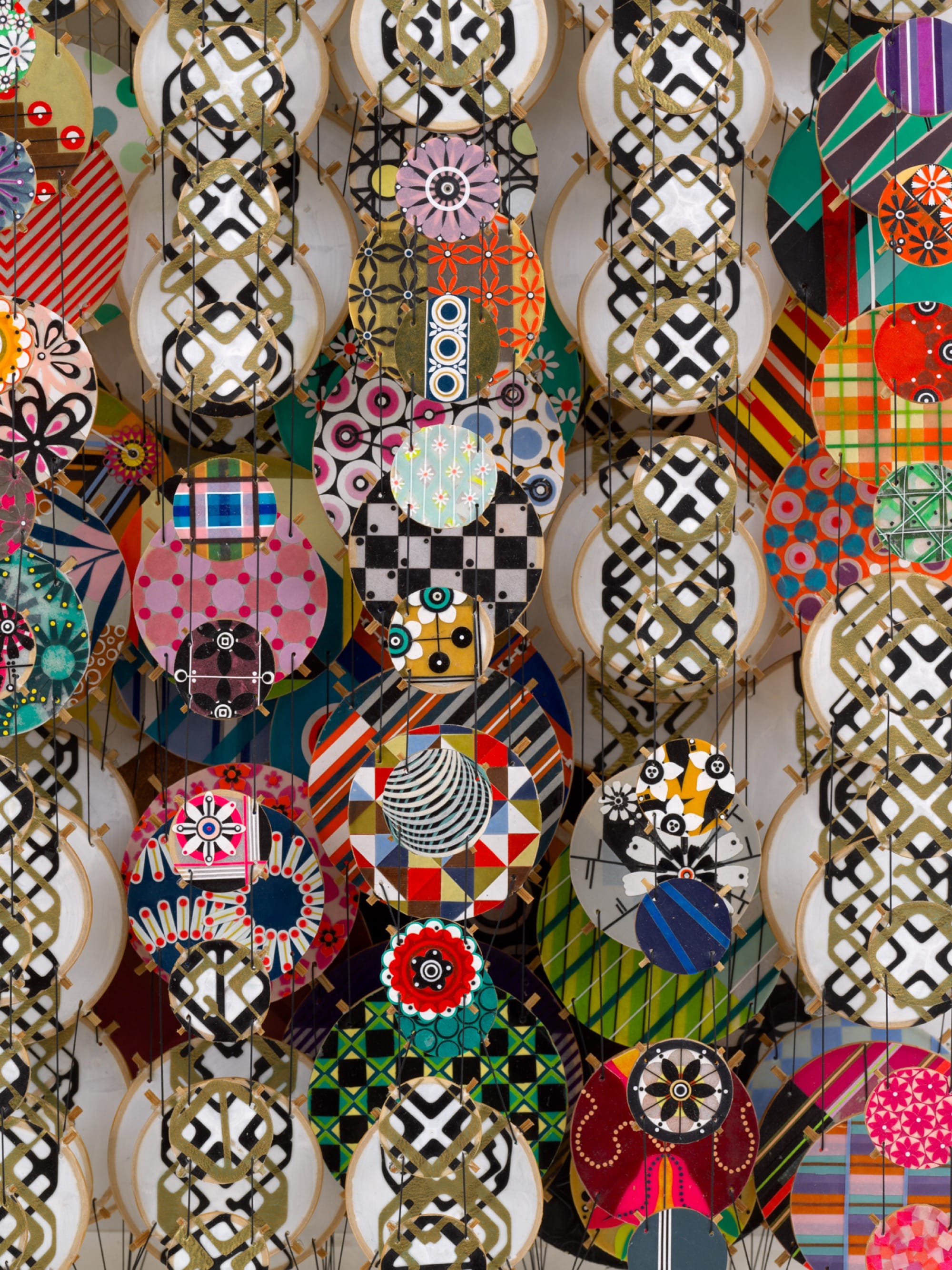 a detail of an abstract artwork by Jacob Hashimoto made from twine and numerous colorful, patterned paper discs installed in rows for a layered effect