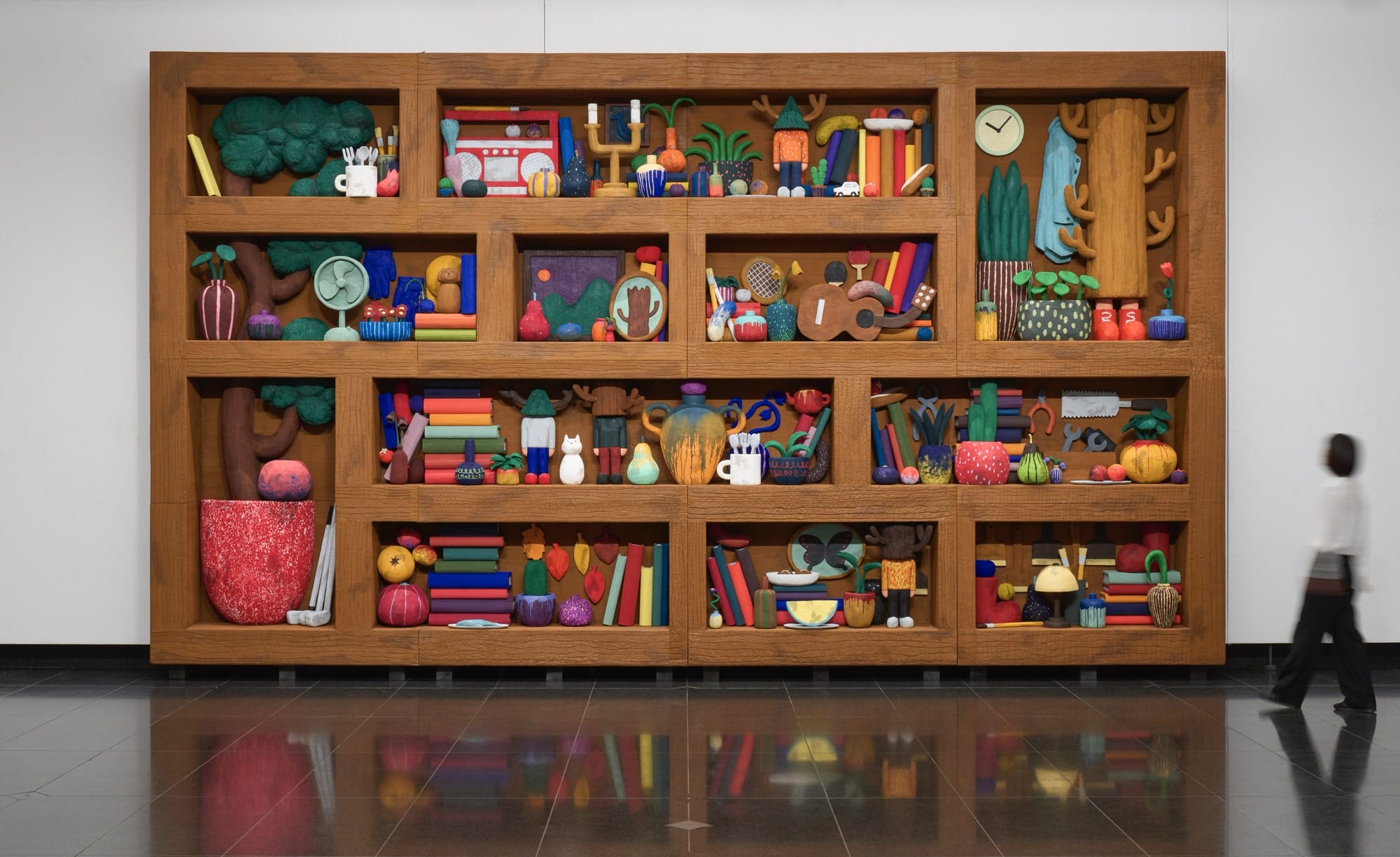 a sculptural installation by Yuichi Hirako of an oversized shelf filled with cartoonish domestic forms like vases, food, candlesticks, and other objects