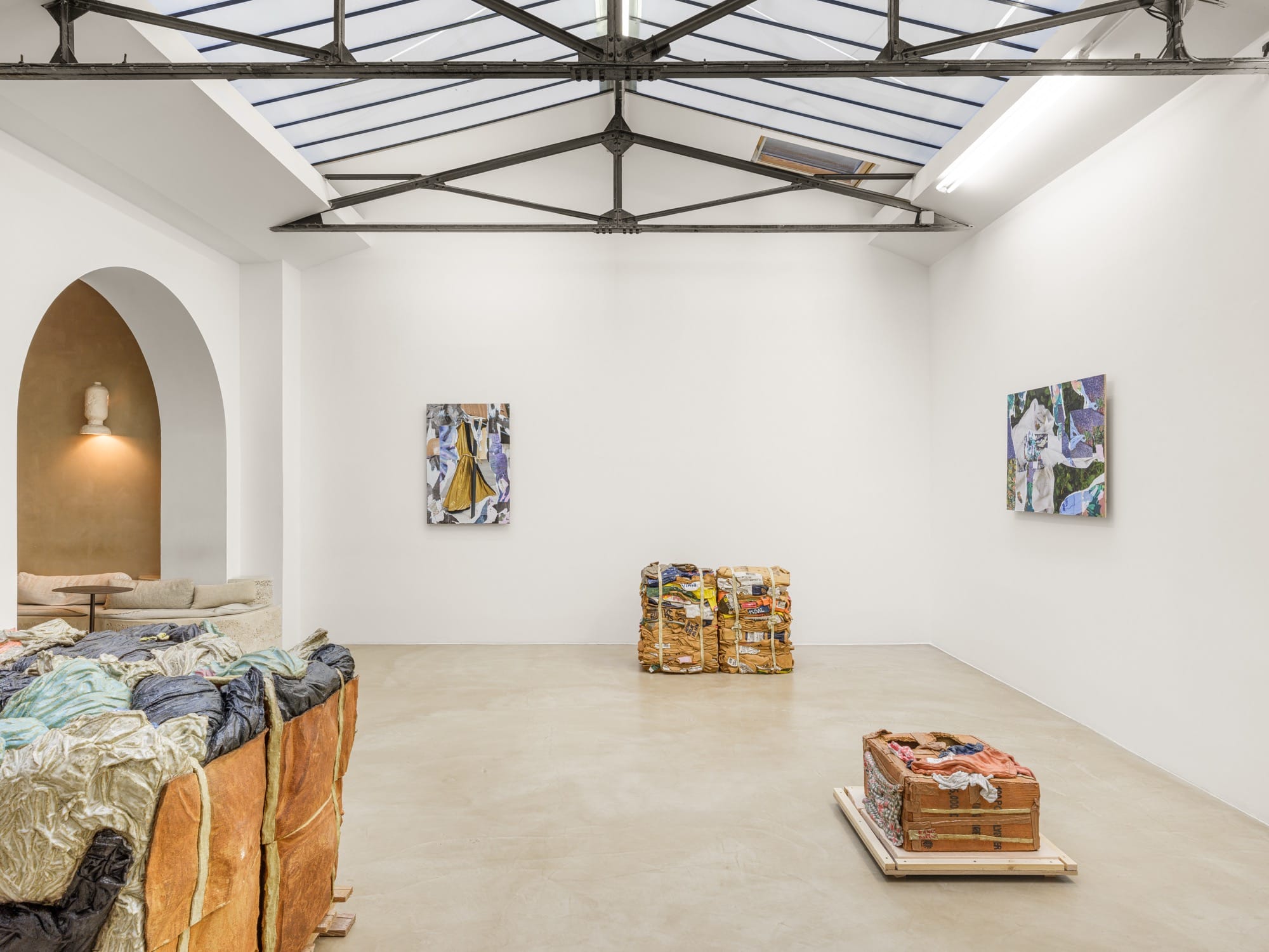 an installation view of an exhibition by Ninon Hivert of glass, bronze, and clay sculpture mimicking stacks of discarded materials like cardboard and clothing