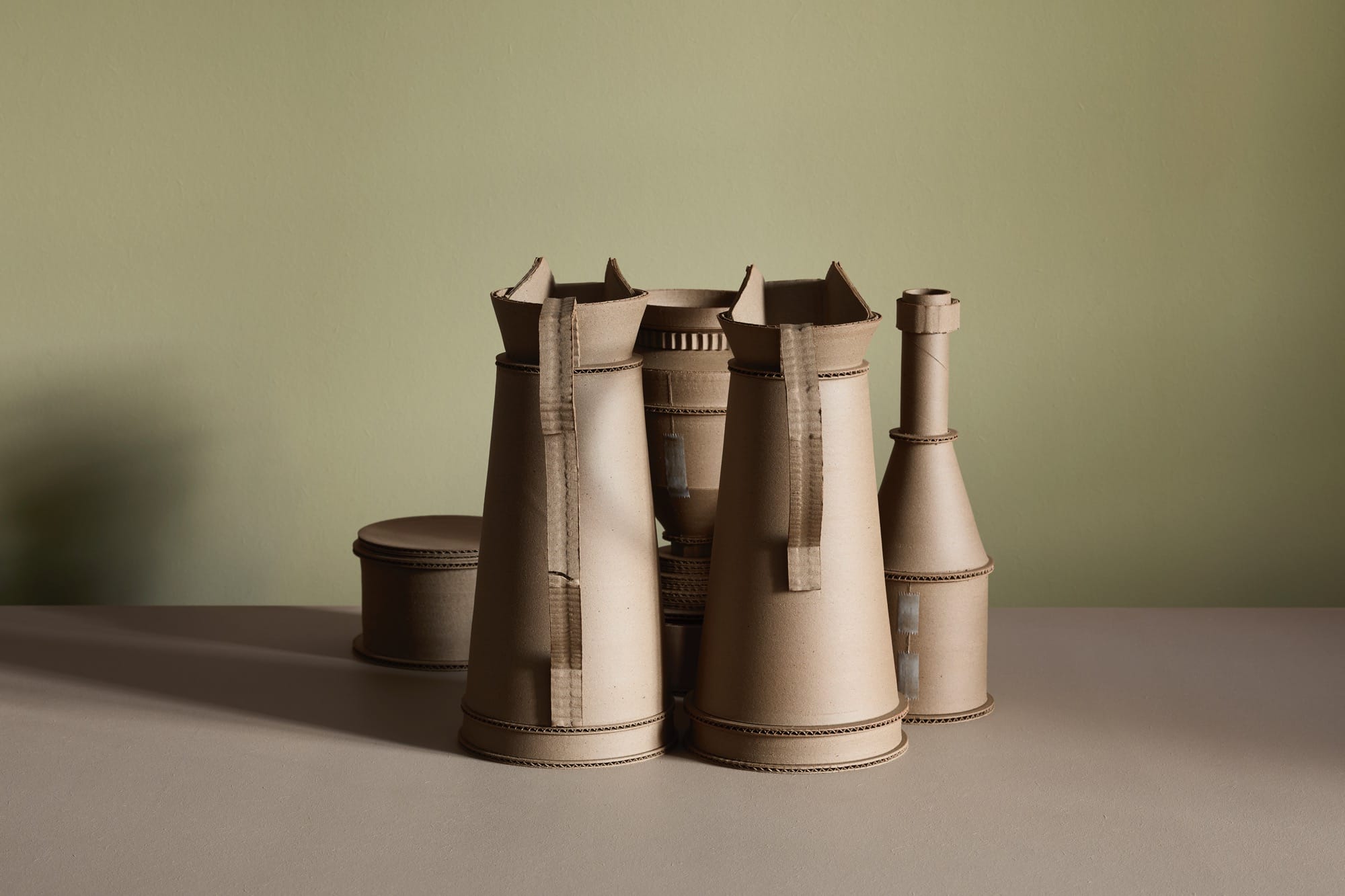 a series of ceramic vessels by Jacques Monneraud that resemble cardboard with tape, arranged to mimic a painting by Giorgio Morandi