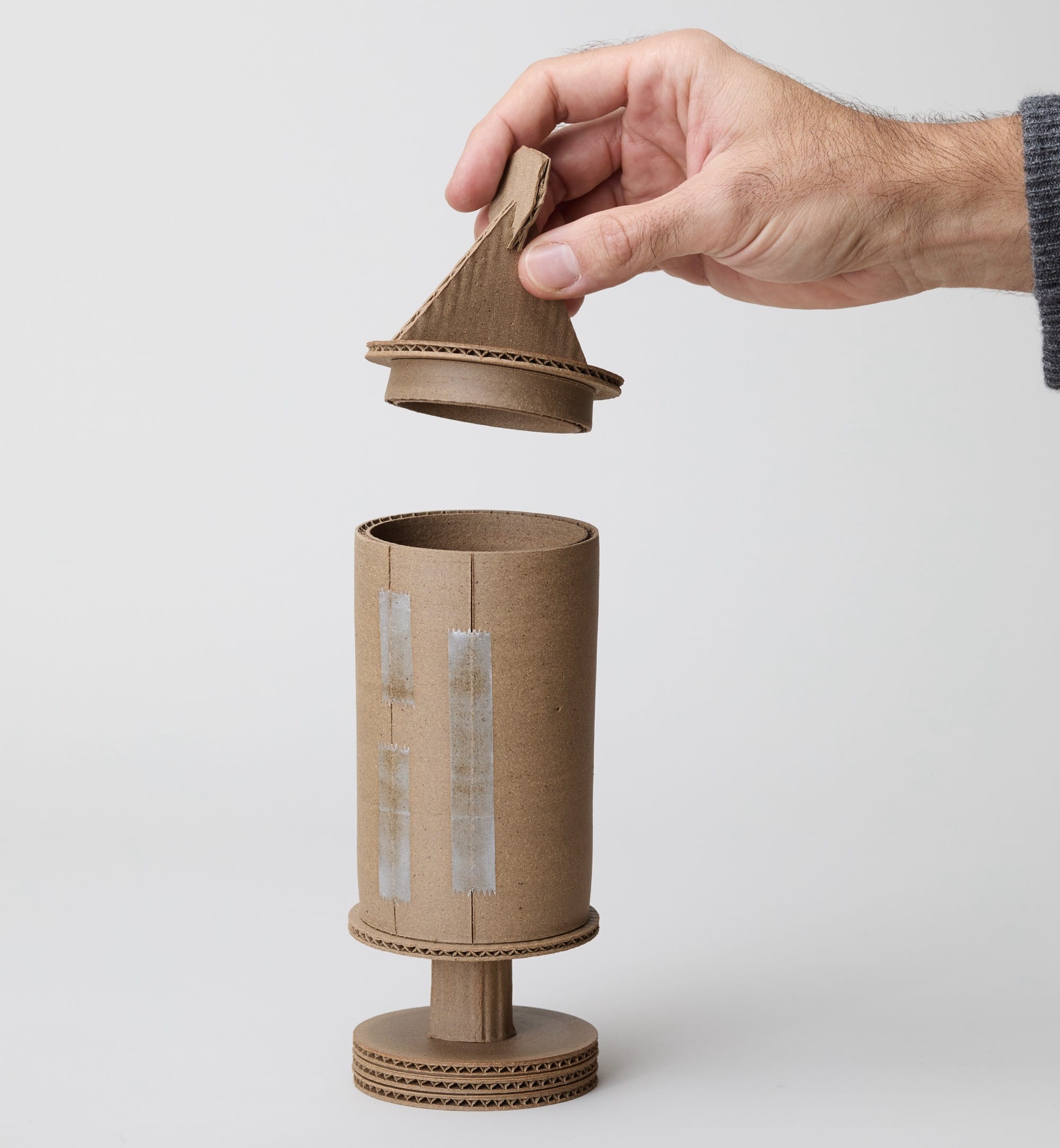 a hand holds the lid of a ceramic sculpture by Jacques Monneraud that resembles cardboard with tape