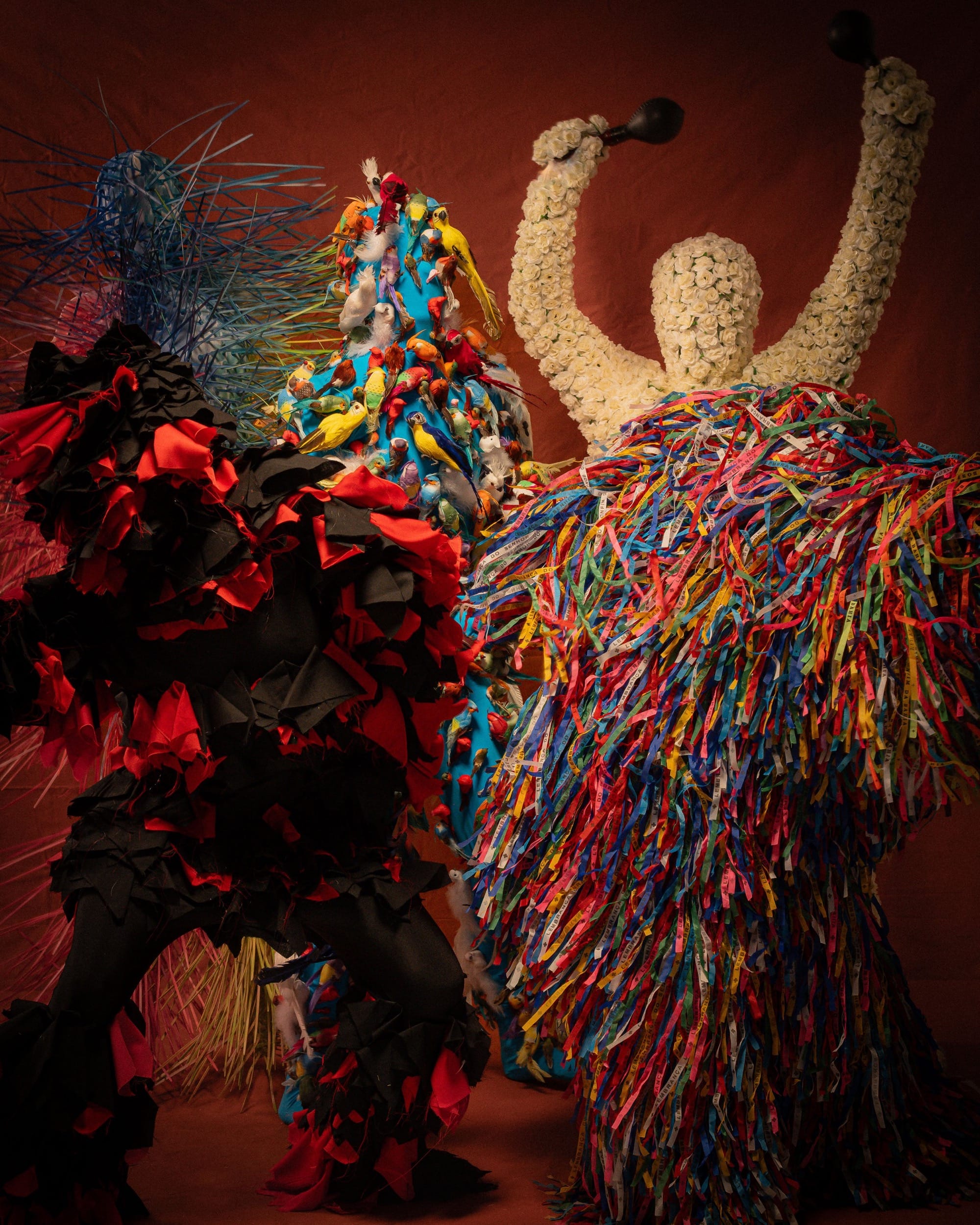 costumed figures in flowers and ribbons dance against a red background