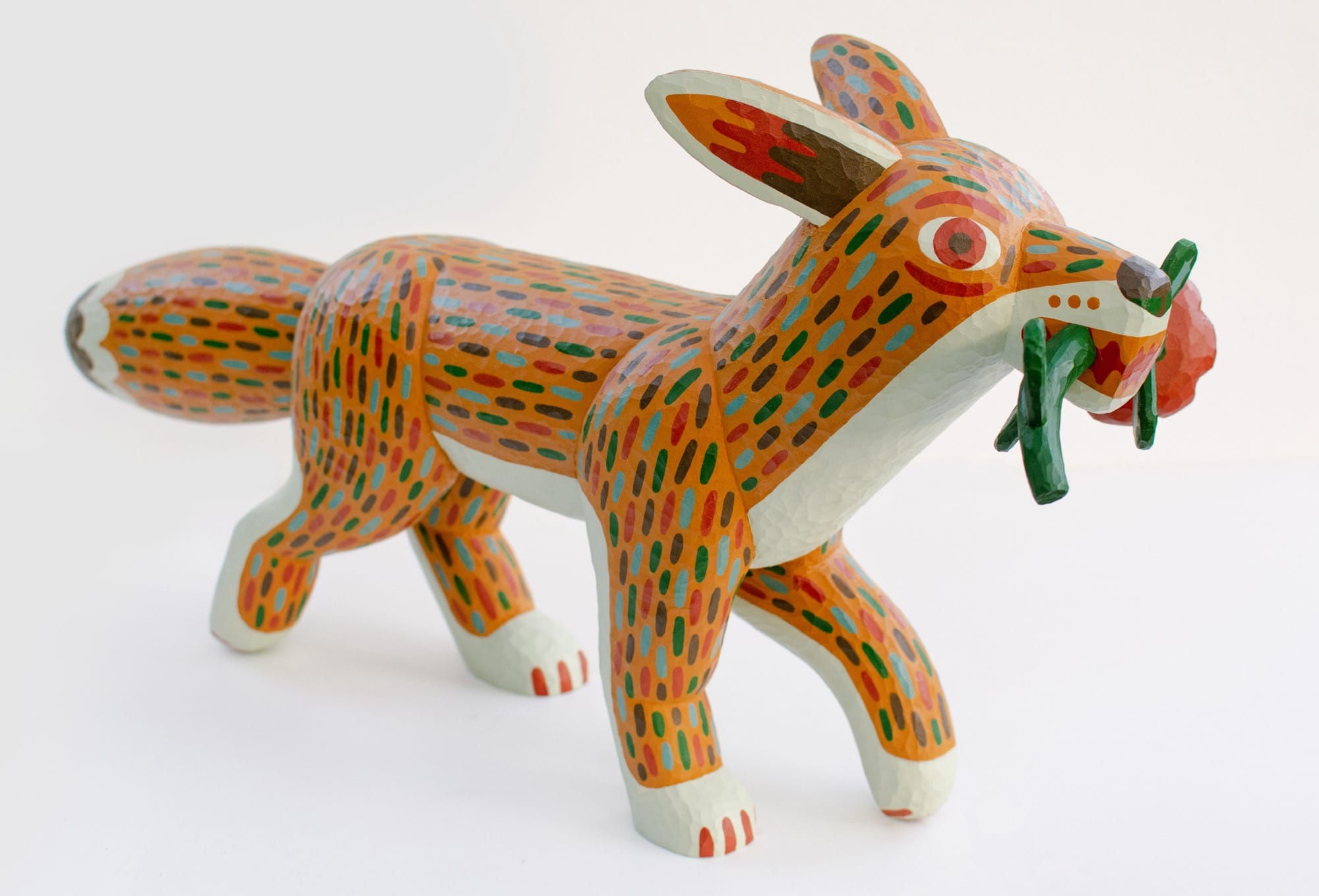 a colorful, hand-carved wooden sculpture of a fox or coyote carrying a flower in its mouth